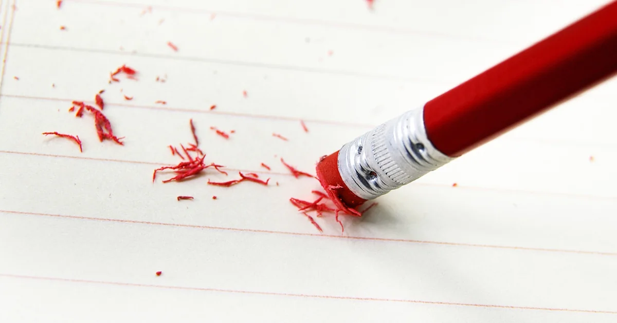 A red pencil with a red eraser erasing an error on a piece of paper